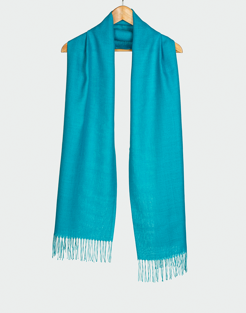 Bufanda color turquesa claro con flecos en los extremos colgada en gancho de madera estilo elegante y ligero