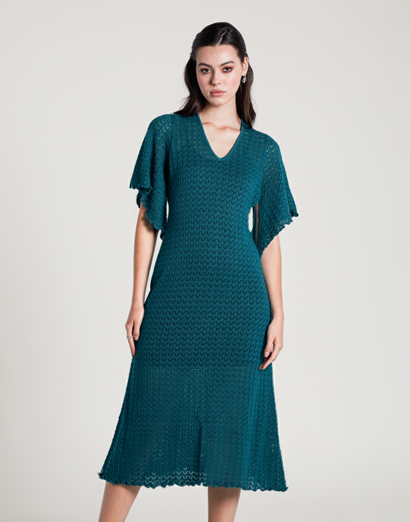 Modelo luciendo un vestido verde teal de tejido calado con escote en V y mangas tipo mariposa, elaborado en algodón orgánico. Diseño elegante y ligero ideal para climas cálidos y ocasiones especiales. Pieza de la propuesta atemporal de Anntarah.