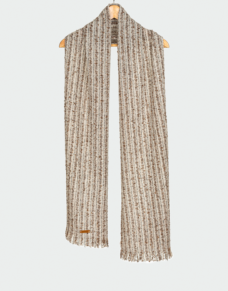 Bufanda acanalada en mezcla de tonos crudo y marrón claro con textura jaspeada y flecos finos colgada en gancho de madera