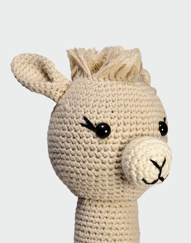 Primer plano de alpaca amigurumi tejida a mano en algodón orgánico color beige con ojos de botón y melena de hilo, diseño decorativo infantil ANNTARAH