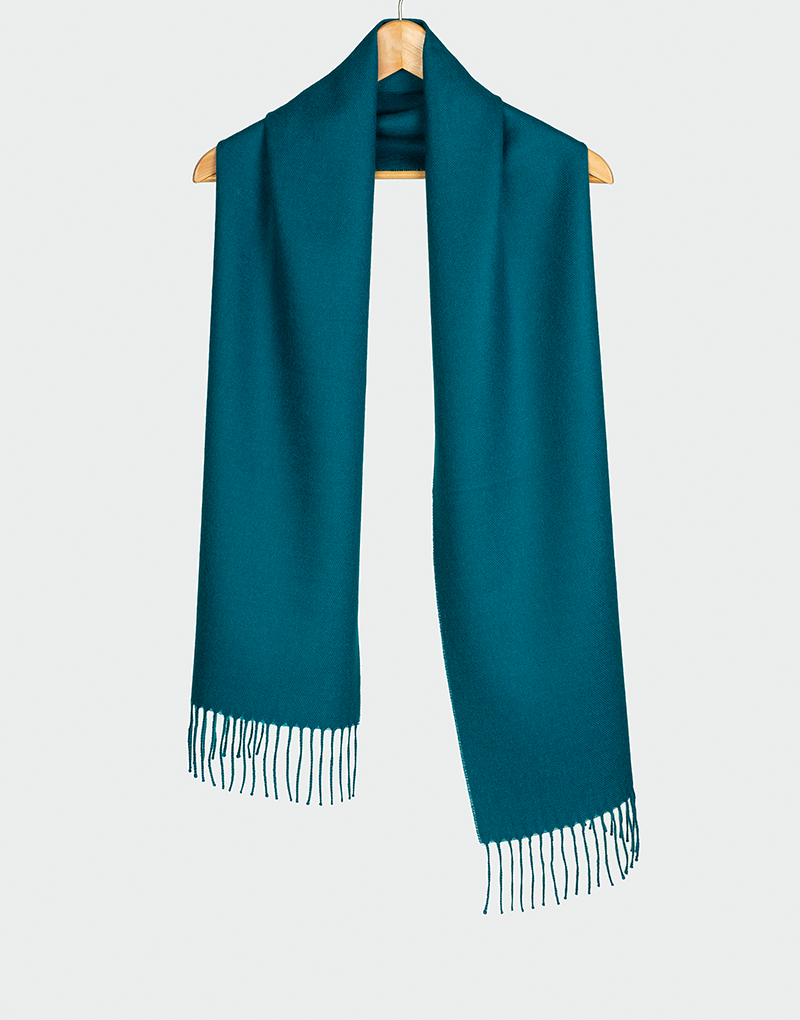 Bufanda azul petróleo con flecos colgada en gancho de madera perfecta para estilos sobrios y contemporáneos