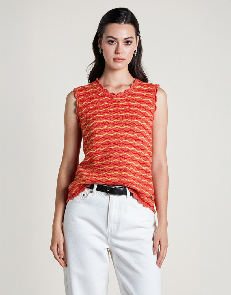 Modelo luciendo el Waves Top de Anntarah en tonos rojos y naranjas con diseño ondulado tejido. Blusa sin mangas de algodón orgánico, con escote redondeado y terminaciones decorativas. Ideal para climas cálidos, con estilo artesanal y elegante.